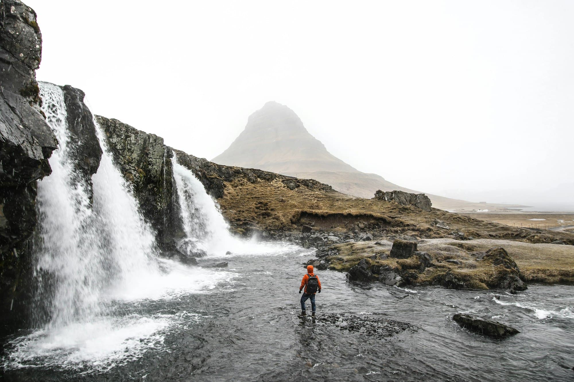 A traveler crossing a river below Kirkjufellsfoss waterfall, Iceland